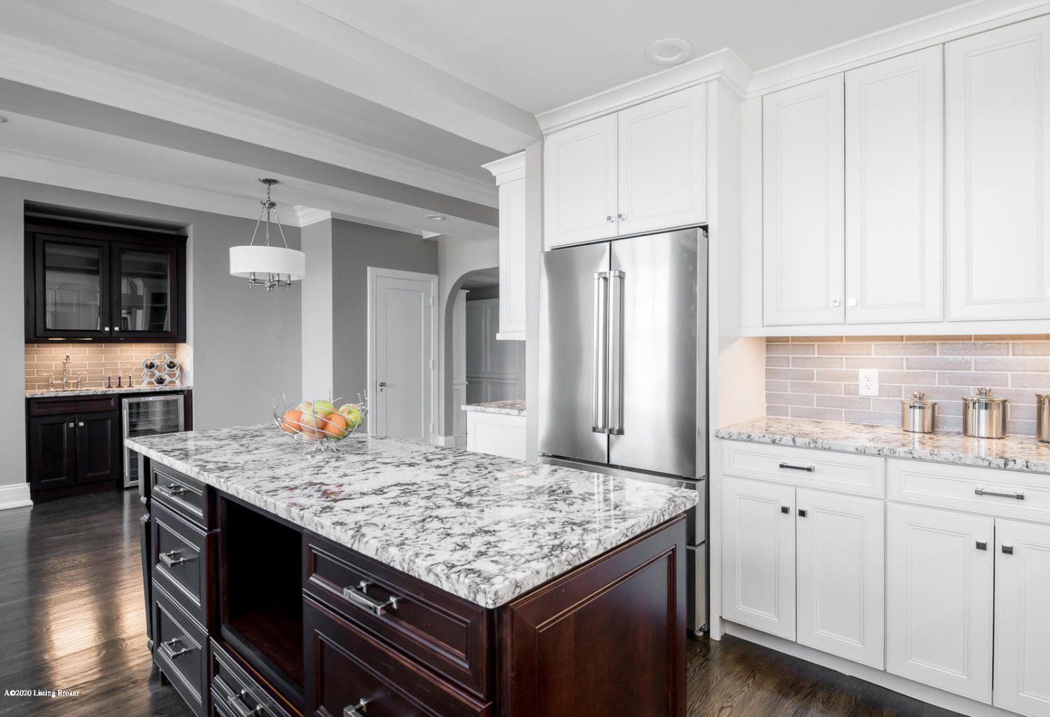 Kitchen with white cabinets, dark island with granite countertop, stainless steel refrigerator.