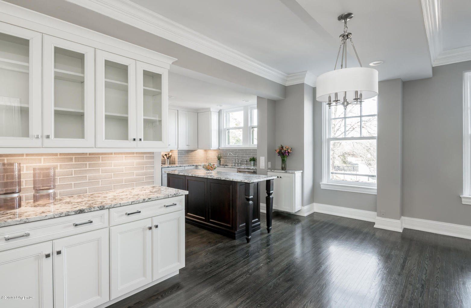 Spacious, white kitchen with dark wood floors, granite countertops, and a central island.