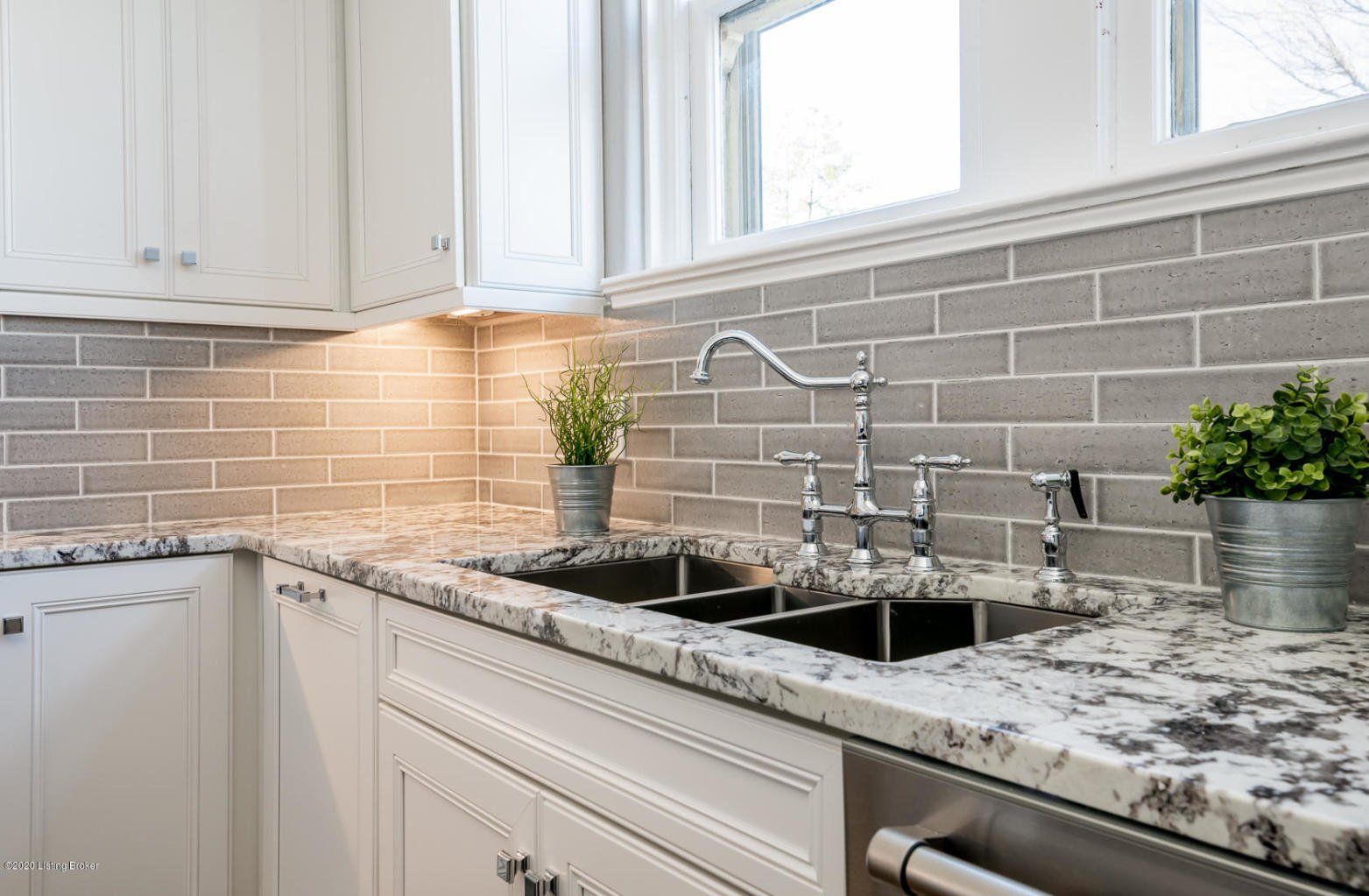 Kitchen with white cabinets, gray brick backsplash, granite countertop, and silver faucet.