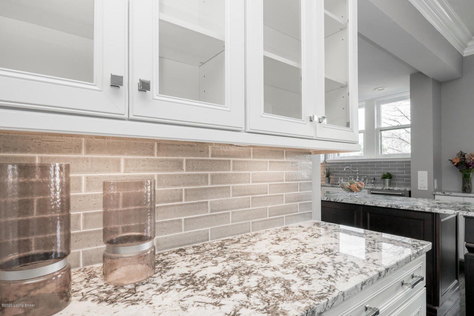 White kitchen cabinets above a granite countertop with glass jars.