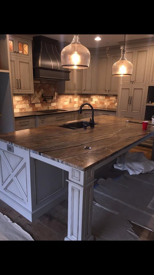 Kitchen with island, light cabinets, dark countertops, pendant lights, and stainless steel range hood.