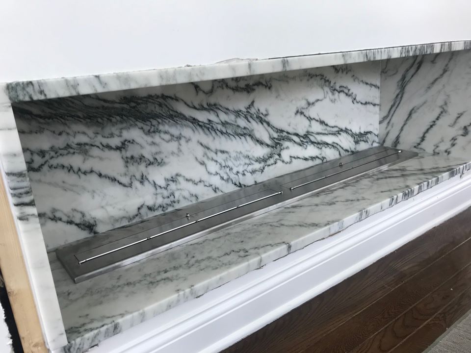Marble fireplace mantel with gray veining and a stainless steel linear insert beneath a white shelf