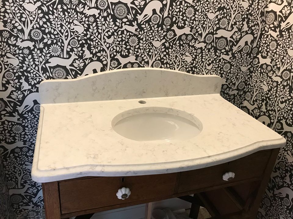 Bathroom vanity with white sink countertop and brown cabinet against patterned wallpaper