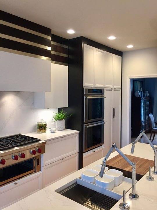 Modern white kitchen with island sink, built-in ovens, gas range, and dark ceiling accents