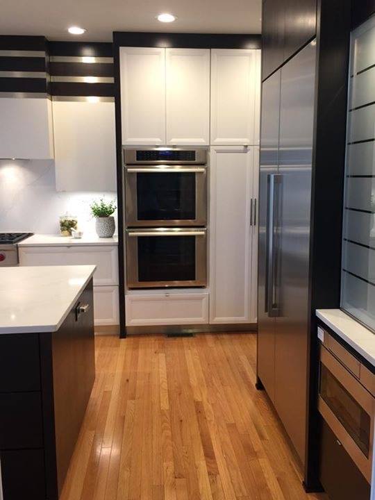 Modern kitchen with white and dark cabinetry, stainless steel appliances, and wooden flooring.
