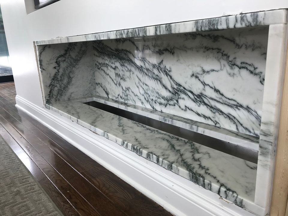Rectangular niche in wall with marble interior, dark veining, and linear drain. White trim surrounds.