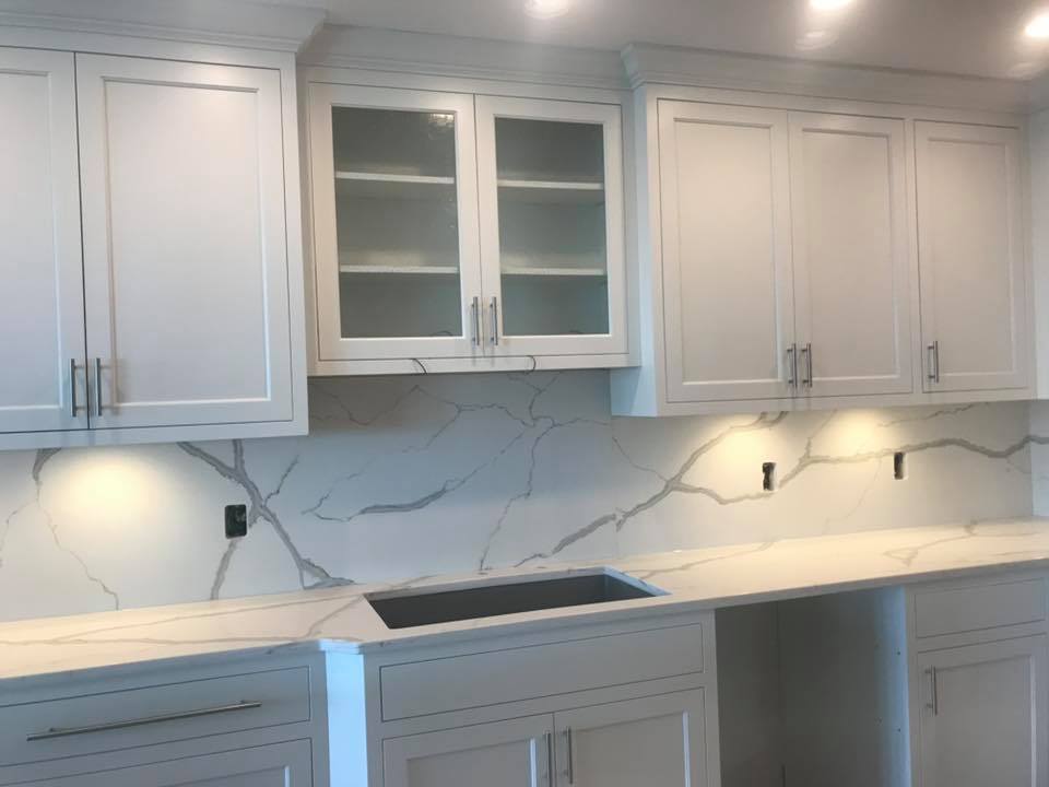 White kitchen cabinets with light countertops and a marble backsplash.