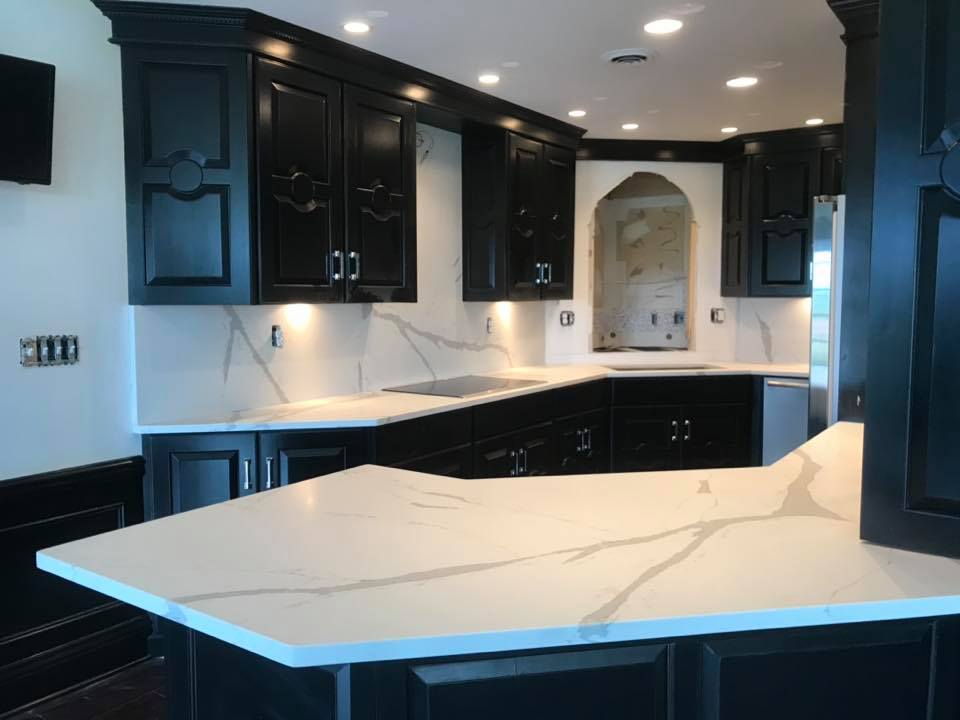 Modern kitchen with black cabinets, white marble countertops, and recessed ceiling lights