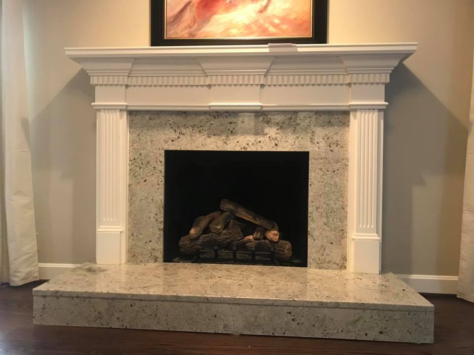 Fireplace with white mantel, speckled gray surround, and dark firebox with logs.