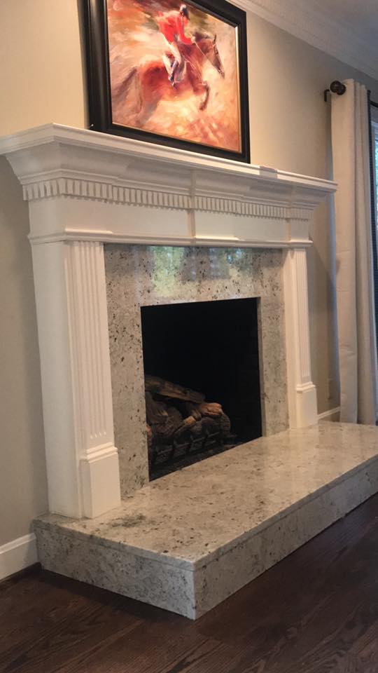 White mantel fireplace with gray speckled granite surround and hearth; art above.
