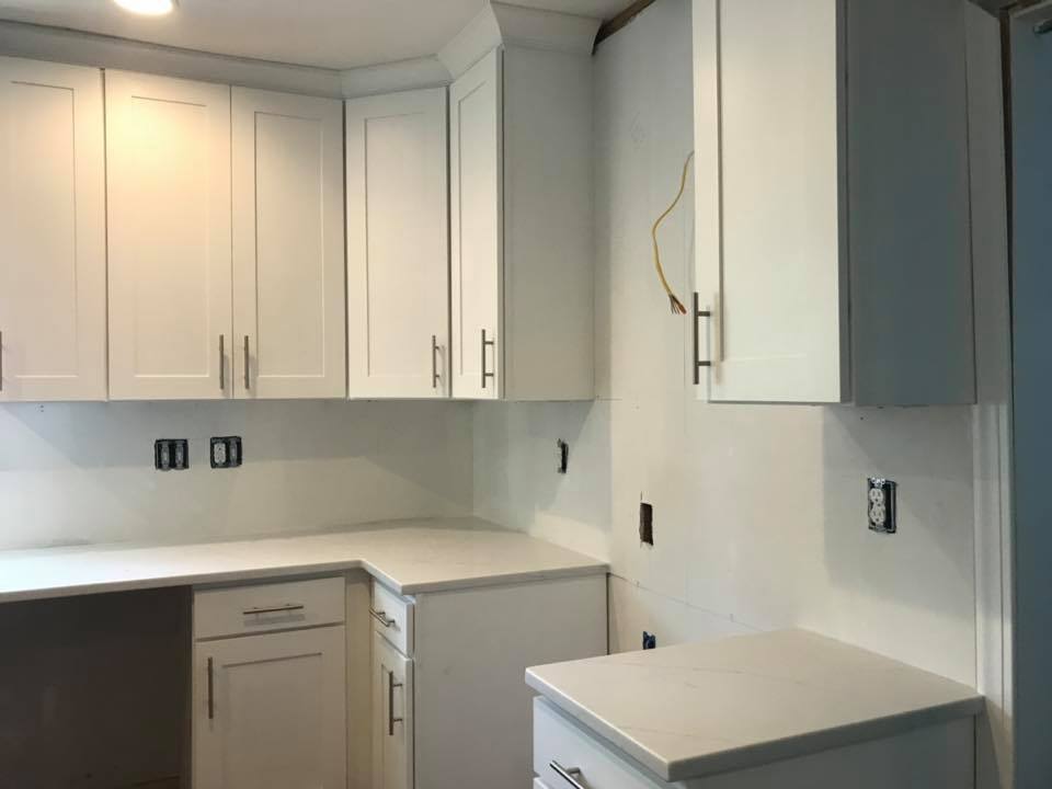 White kitchen with upper and lower cabinets, countertops, and unfinished wall outlets under renovation