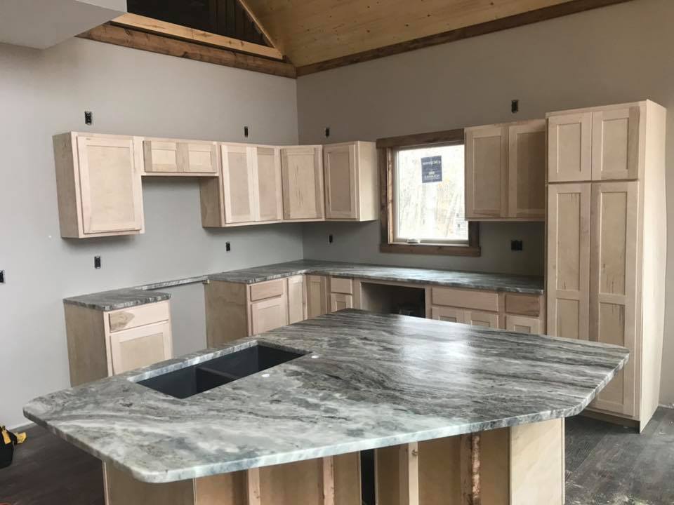 Unfinished kitchen remodel with light wood cabinets, granite countertops, and island with a sink.