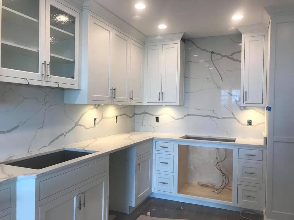 White kitchen cabinets and countertops with marble backsplash. Under-cabinet lighting installed.