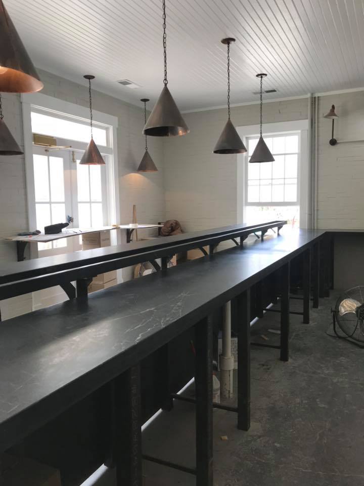 Long, black countertop with pendant lights and windows in a light-colored room.