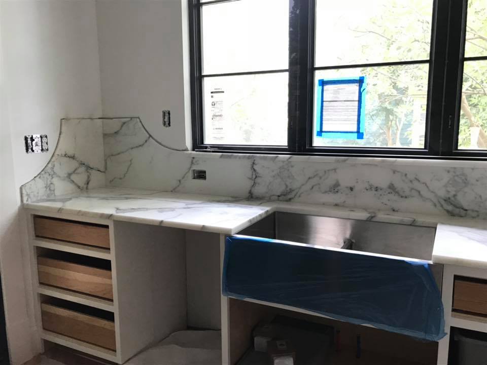 Kitchen under construction with marble countertops, stainless steel sink, and a black-framed window.