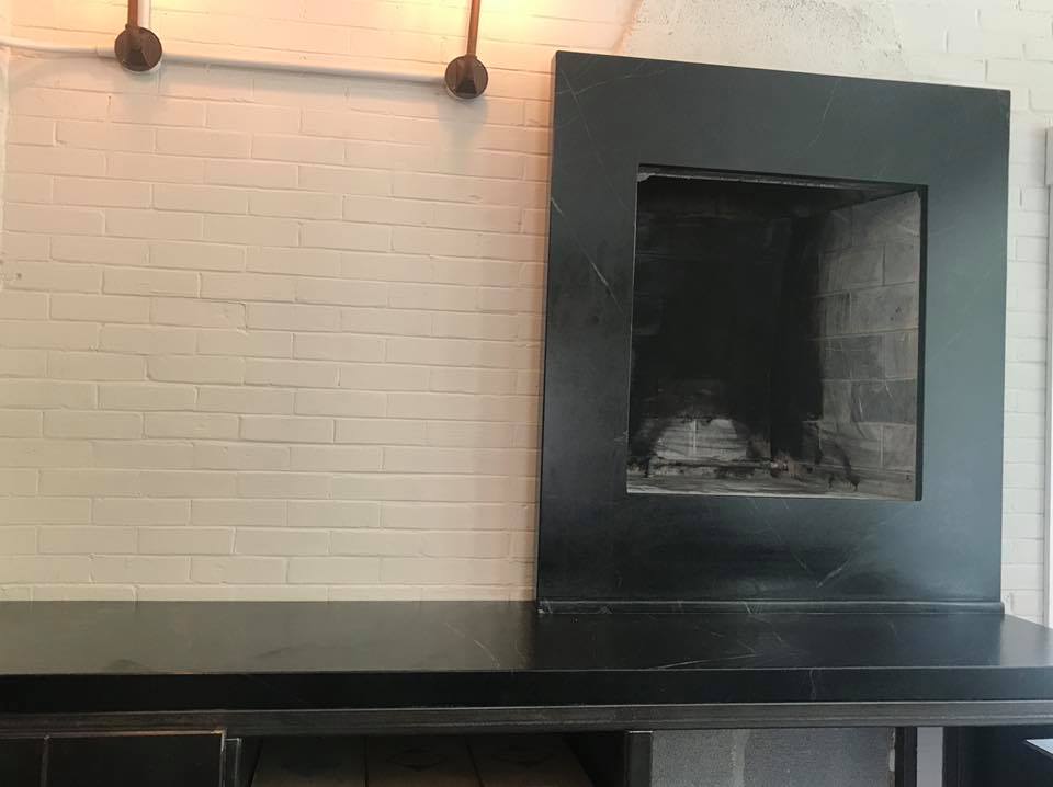 Black fireplace with a rectangular opening set against a white brick wall and black counter.