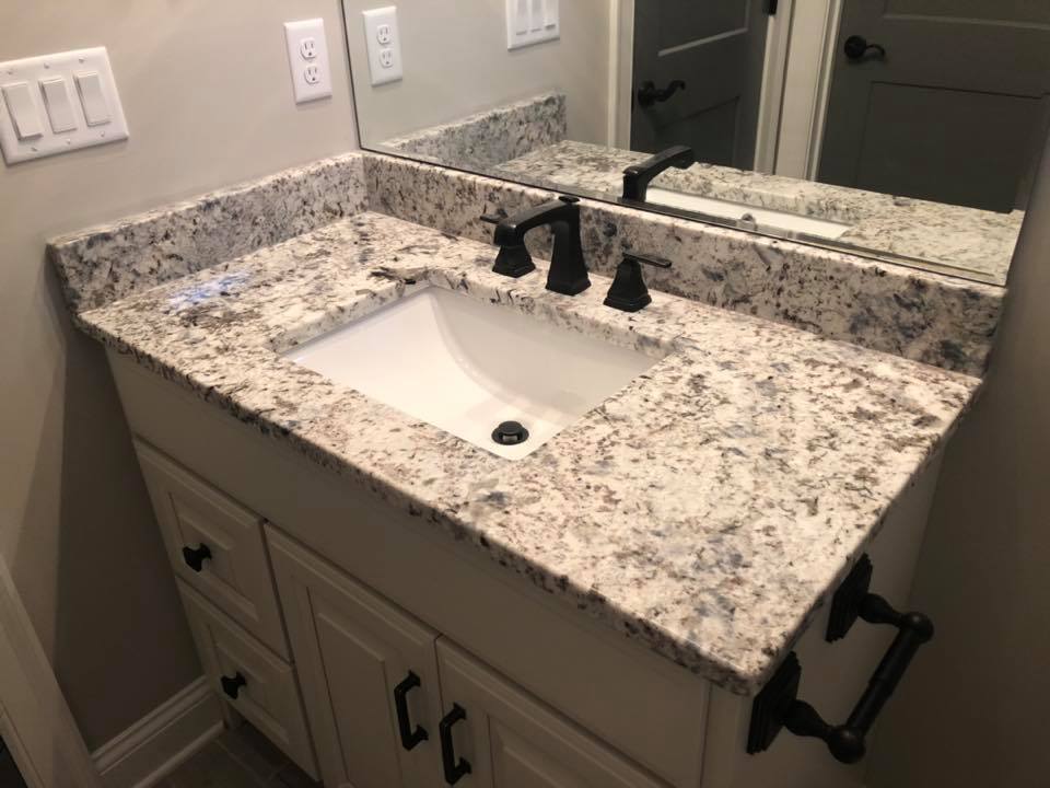 Bathroom vanity with speckled granite countertop, white sink, and black faucet above beige cabinets