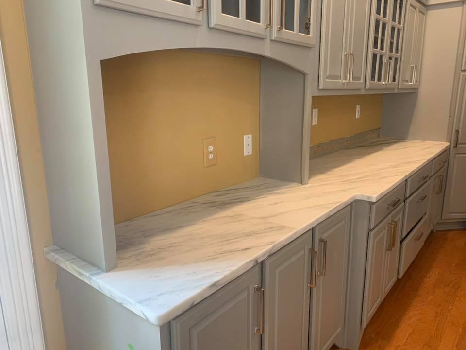 Gray kitchen cabinets with a white marble countertop and a yellow backsplash.