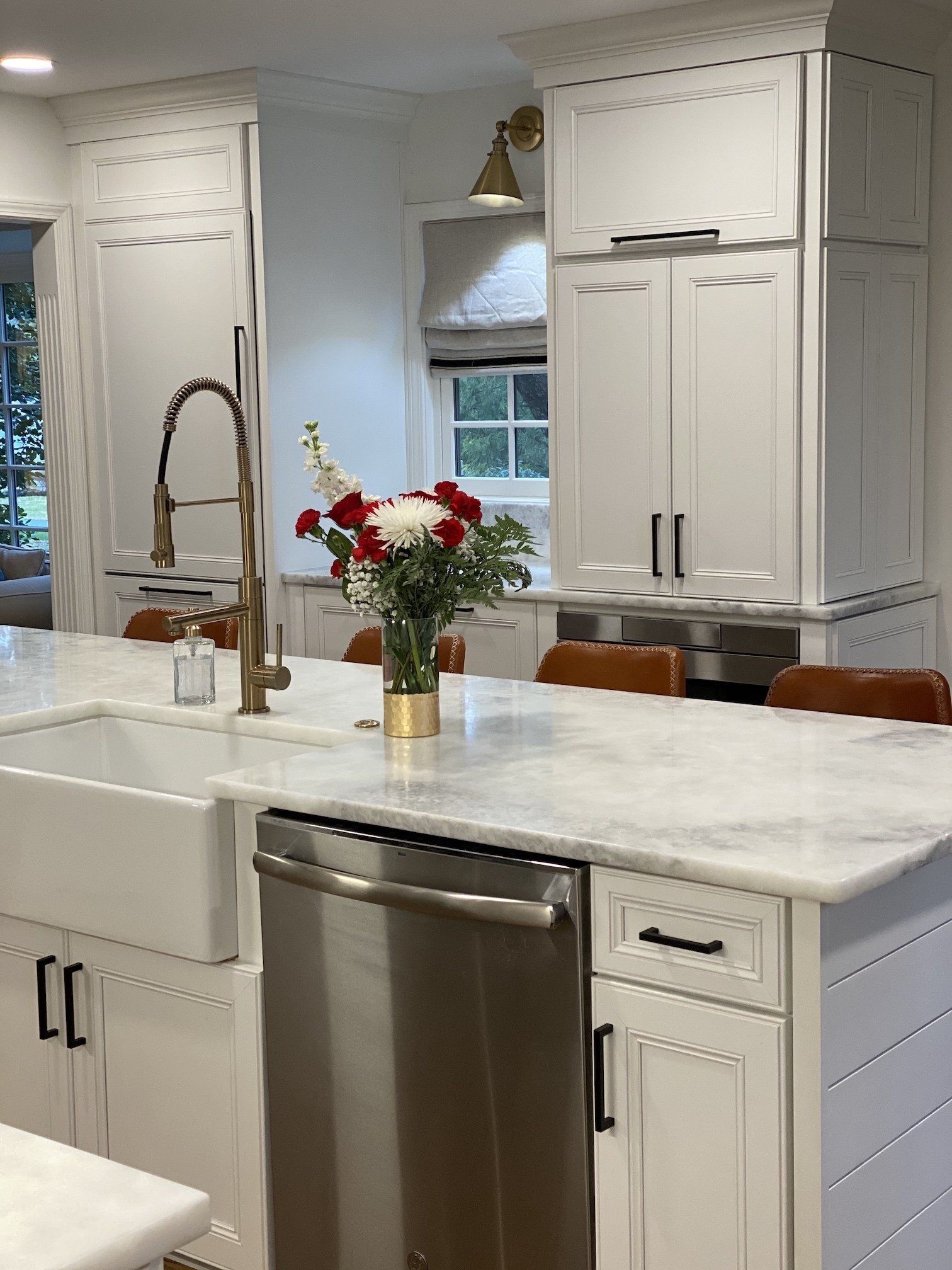 Bright white kitchen with marble island, stainless dishwasher, and vase of red and white flowers
