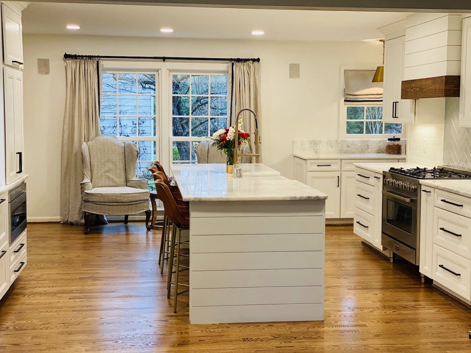 Bright white kitchen with island, wood floor, window, and chair.