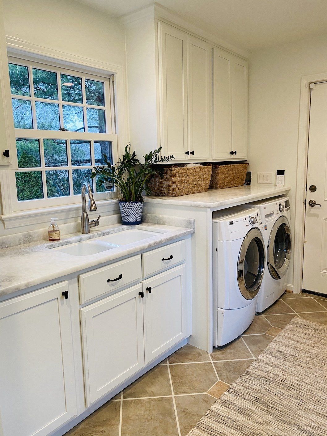 Laundry room with white cabinets, marble countertop, and a window; washer and dryer in place.