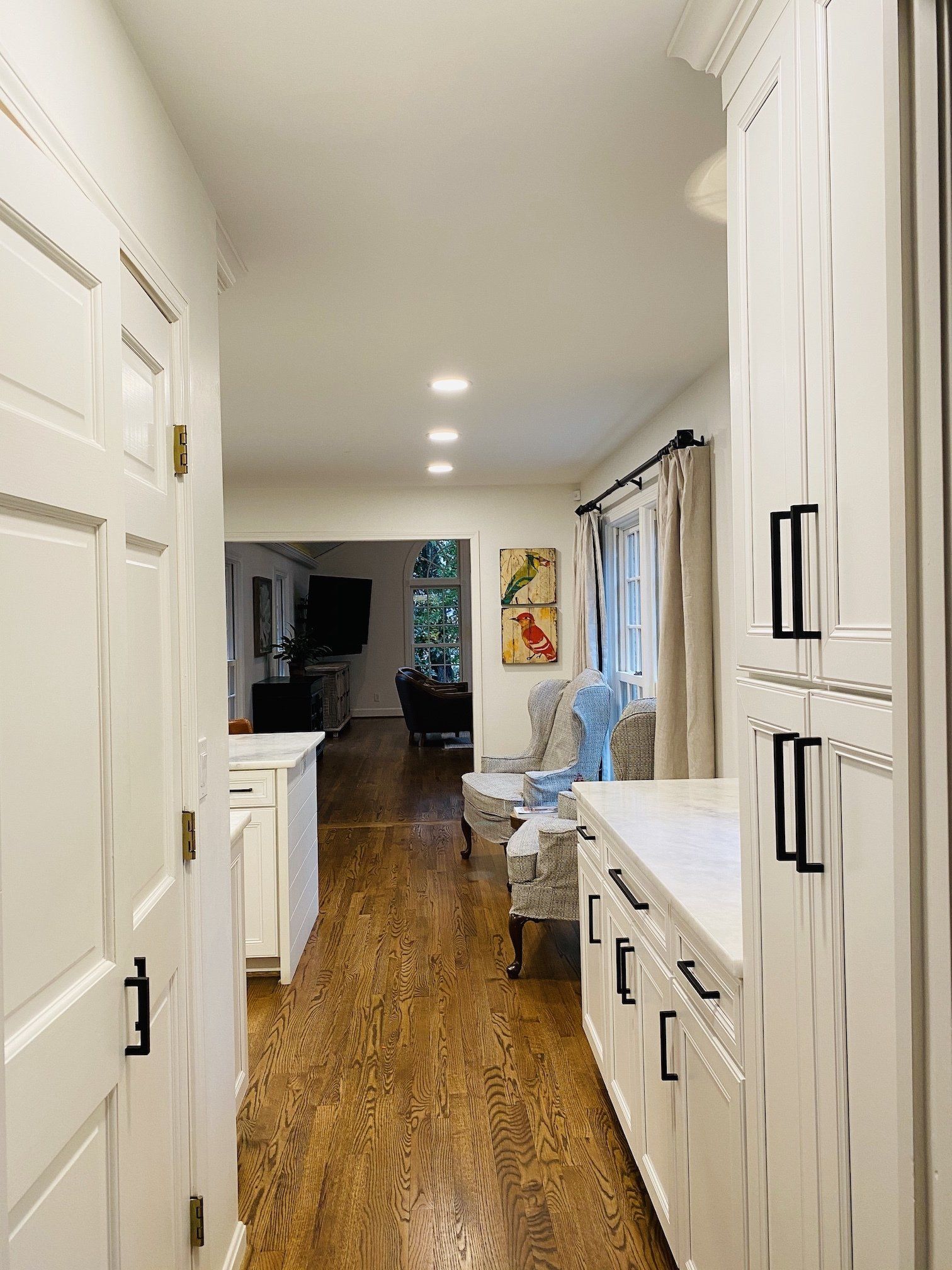 Hallway with white cabinets, wood floors, leading to a living room with seating and artwork.