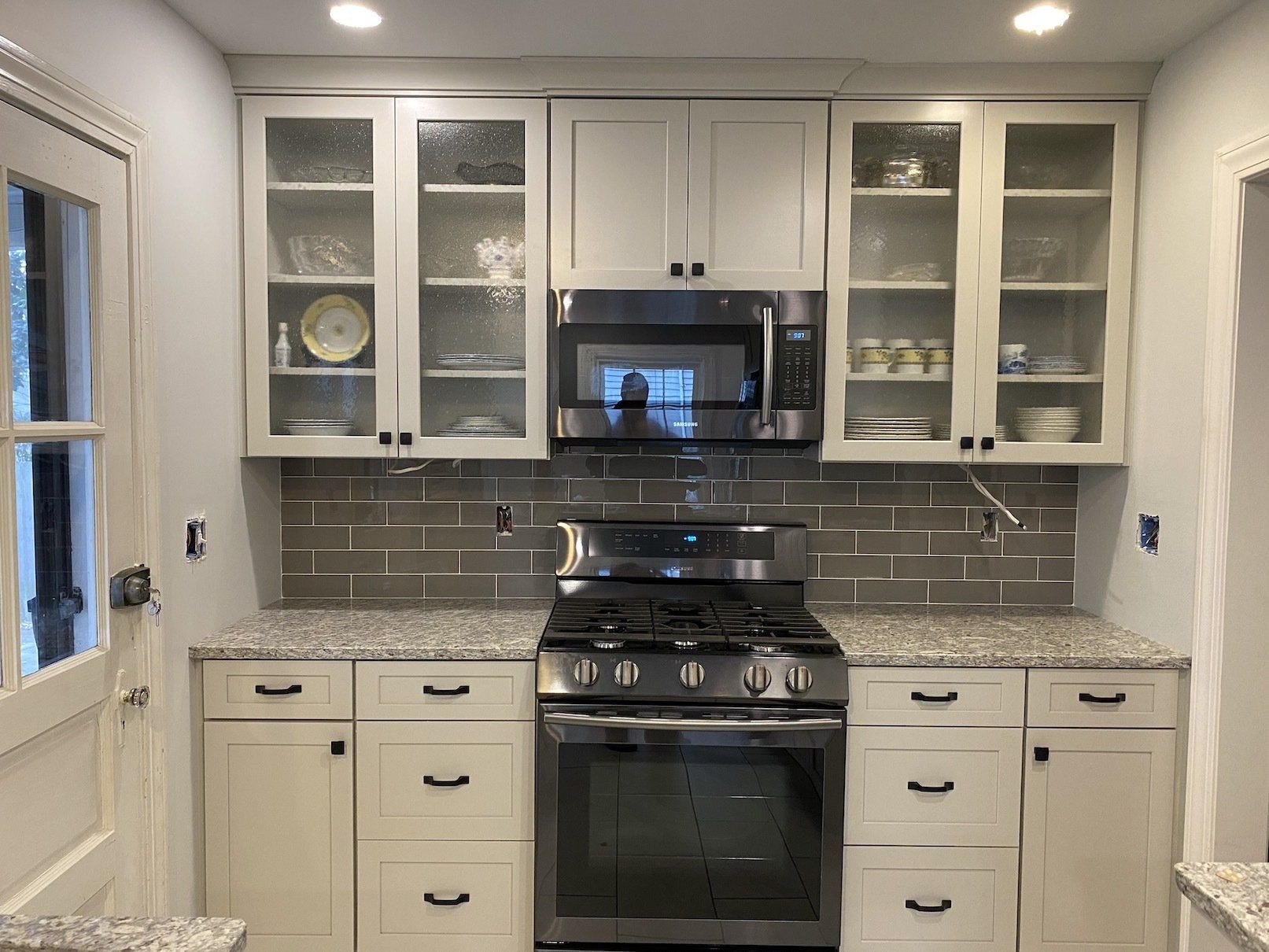 Newly renovated kitchen with white cabinets, stainless steel appliances, and gray tile backsplash.