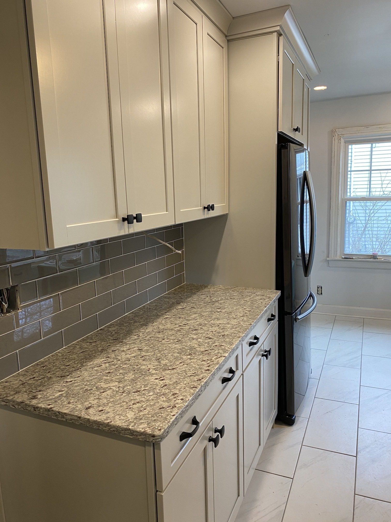 Cream-colored kitchen cabinets with granite countertop and black appliances; a window in the background.