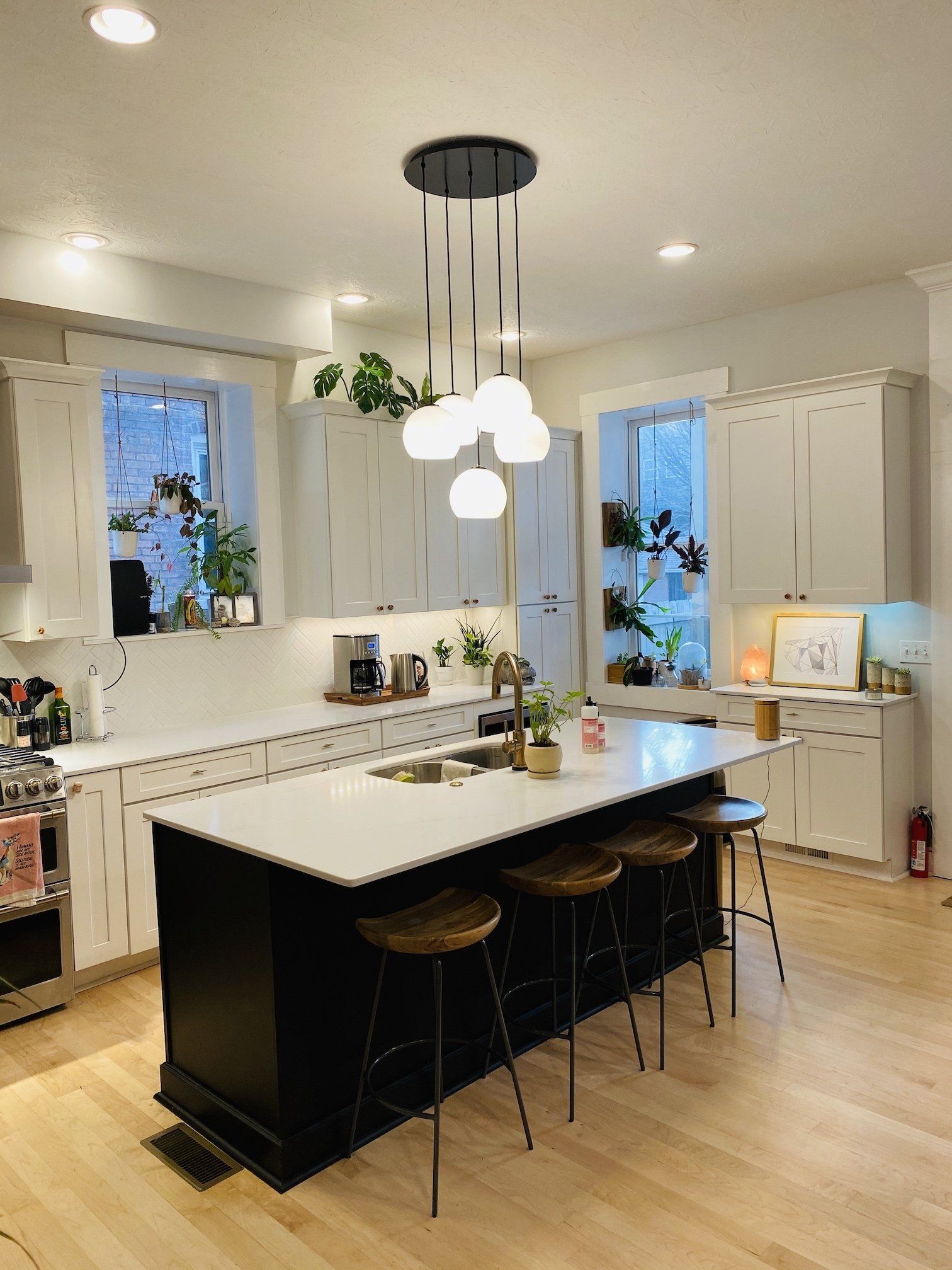 Kitchen with black island, white countertops, globe pendant lights, and potted plants.