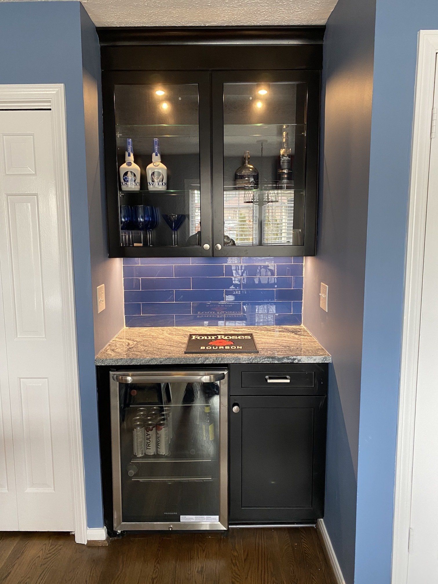 Built-in home bar with a refrigerator, cabinet, lit display case, and blue tile backsplash.