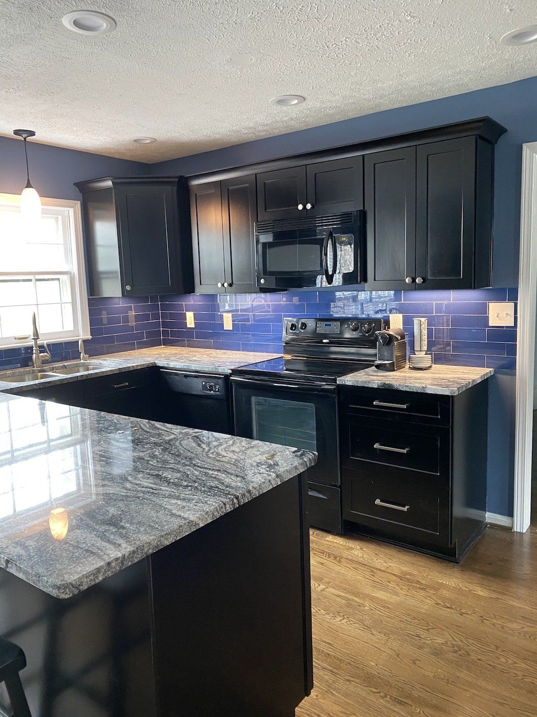 Kitchen with black cabinets, blue backsplash, and granite countertops.