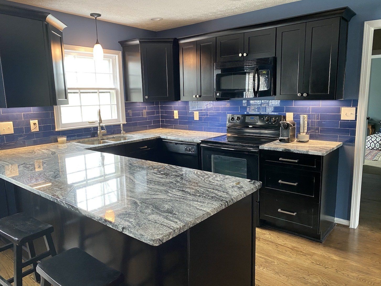 Kitchen with black cabinets, blue backsplash, gray countertops, and a window.