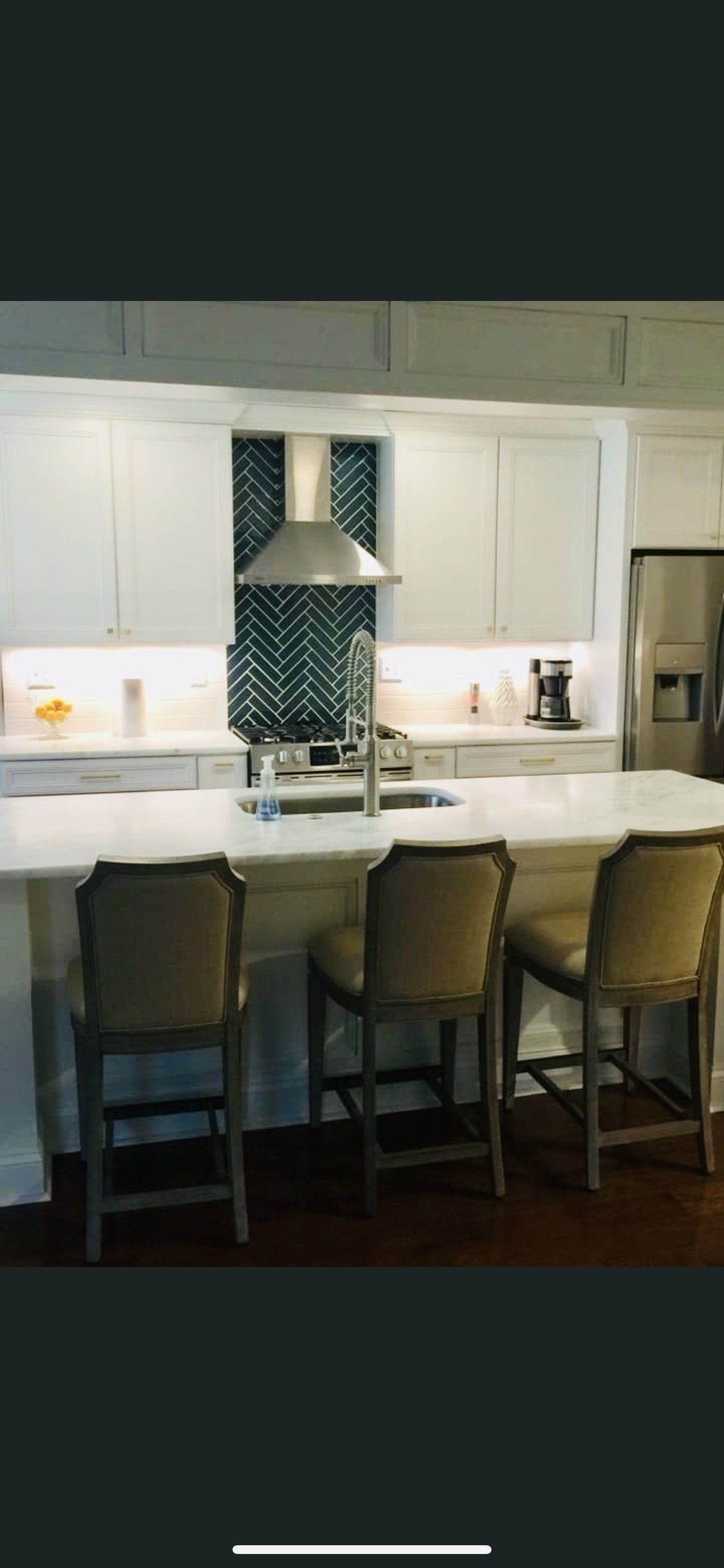 Kitchen island with three bar stools, white cabinets, and a decorative tile backsplash.