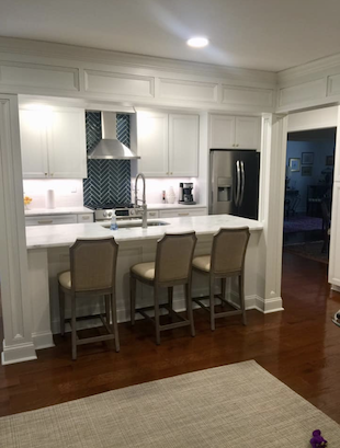 White kitchen with marble countertops, stainless steel appliances, and three beige bar stools.
