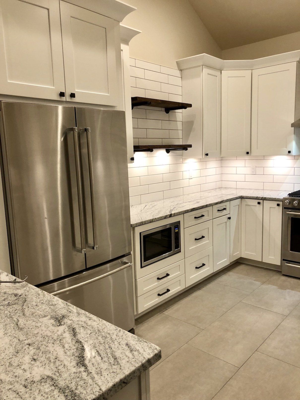 White kitchen with stainless steel appliances, granite countertops, and wood shelves.