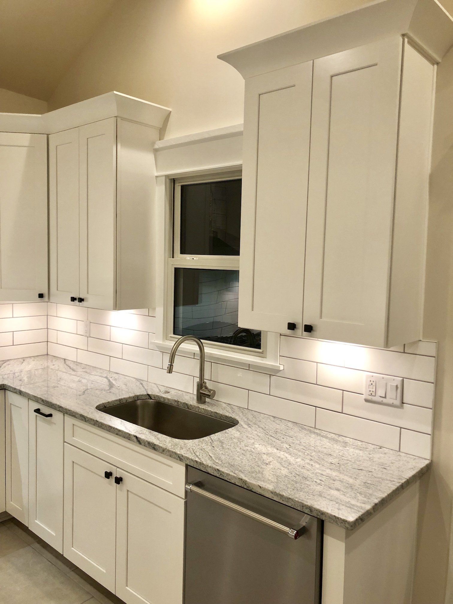 White kitchen with cabinets, granite countertops, subway tile backsplash, and stainless steel sink and dishwasher.
