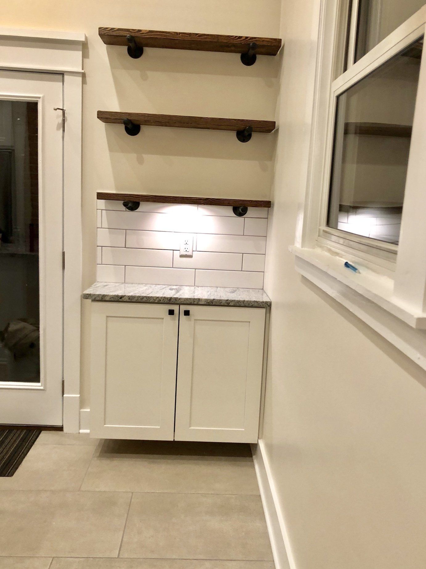 White cabinets with granite countertop, tiled backsplash, and wooden shelves.