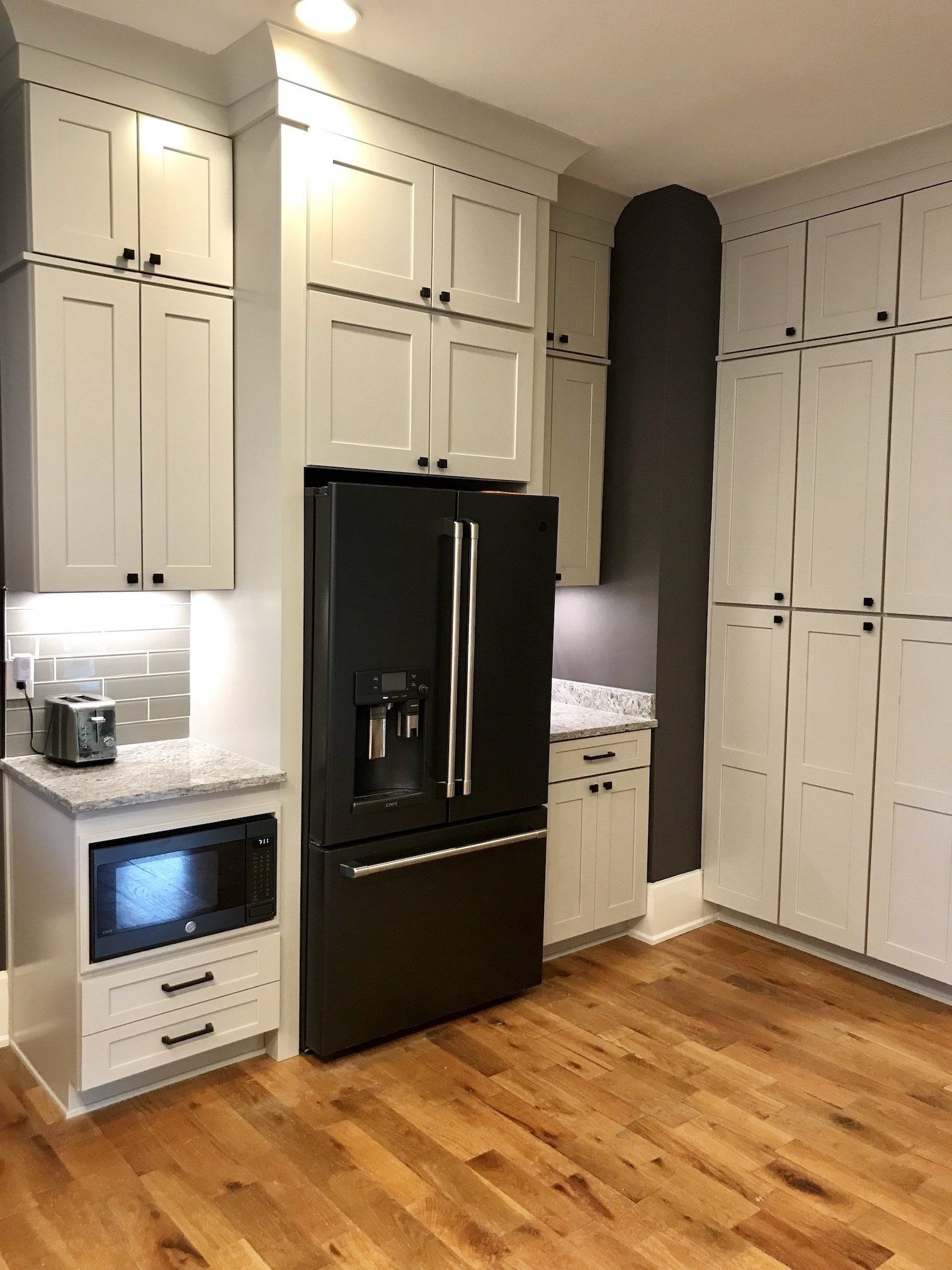 Kitchen with light gray cabinets, black refrigerator, microwave, toaster, and wooden floor.