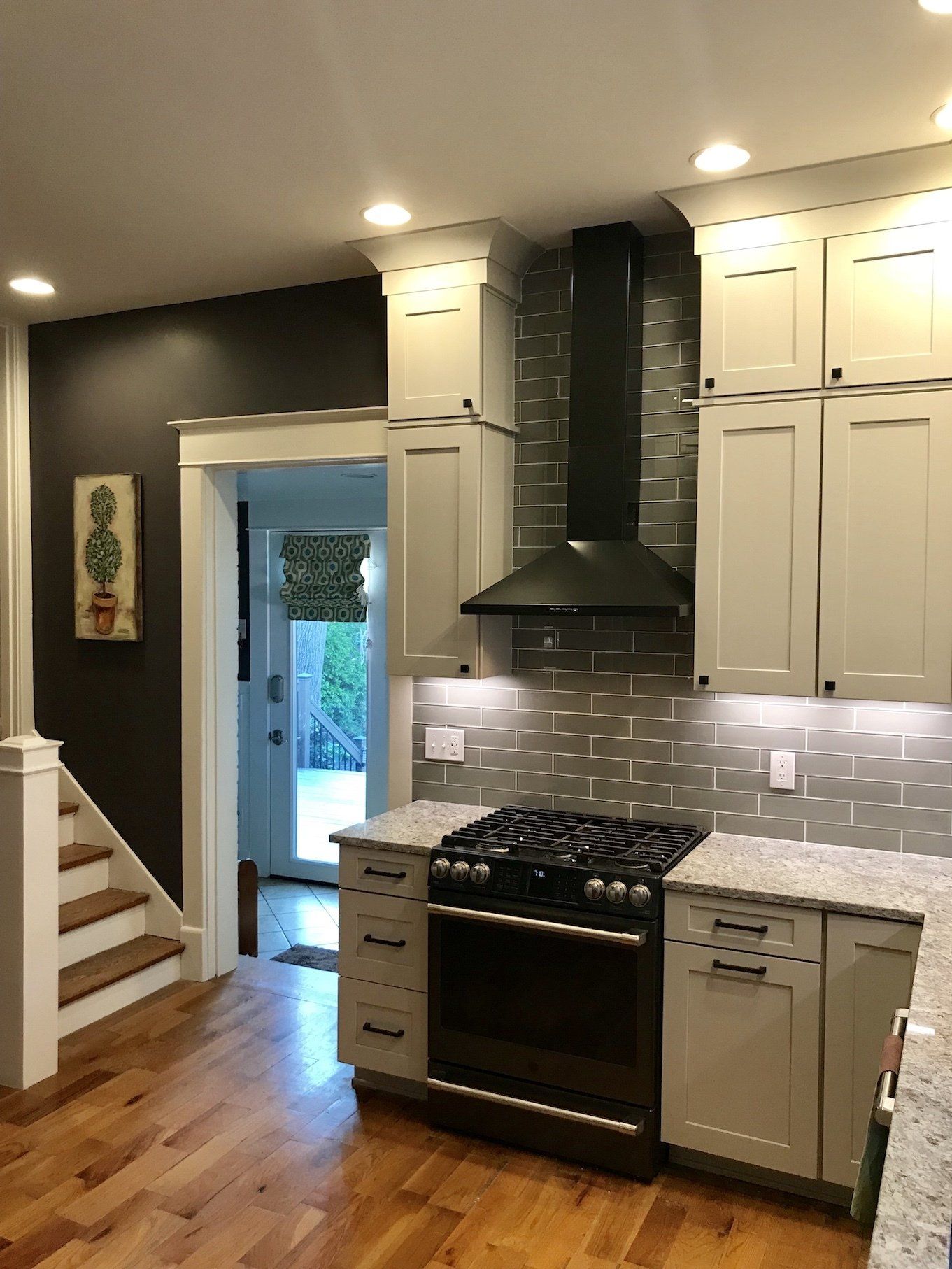 Kitchen with white cabinets, black range, and gray tile backsplash.