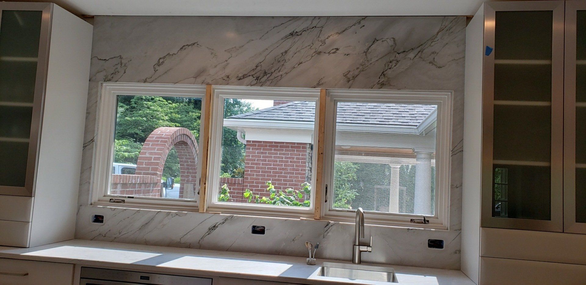 Kitchen with white marble backsplash, three windows, and white cabinets.