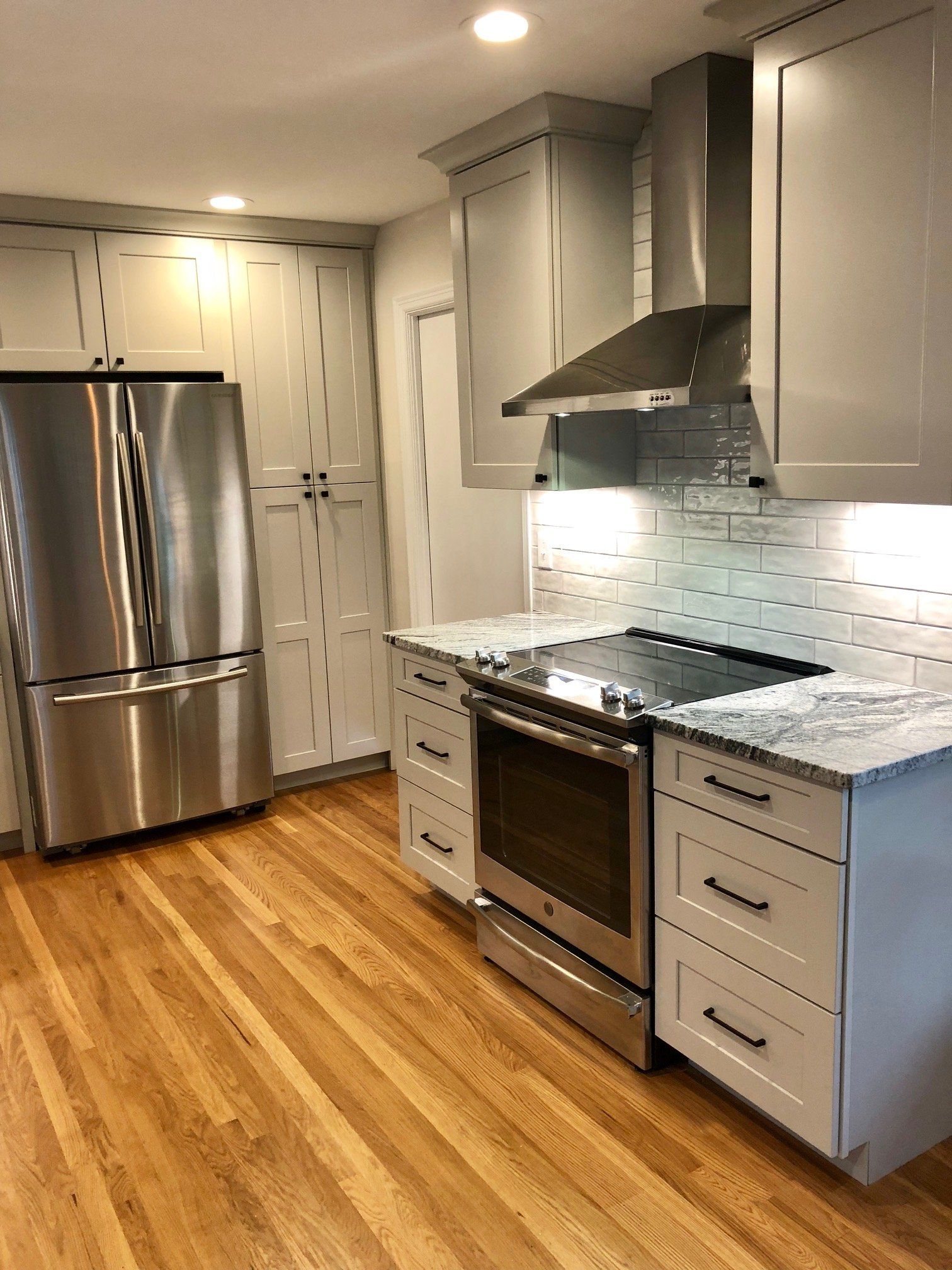 Modern kitchen with light gray cabinets, stainless steel appliances, and wood floors.