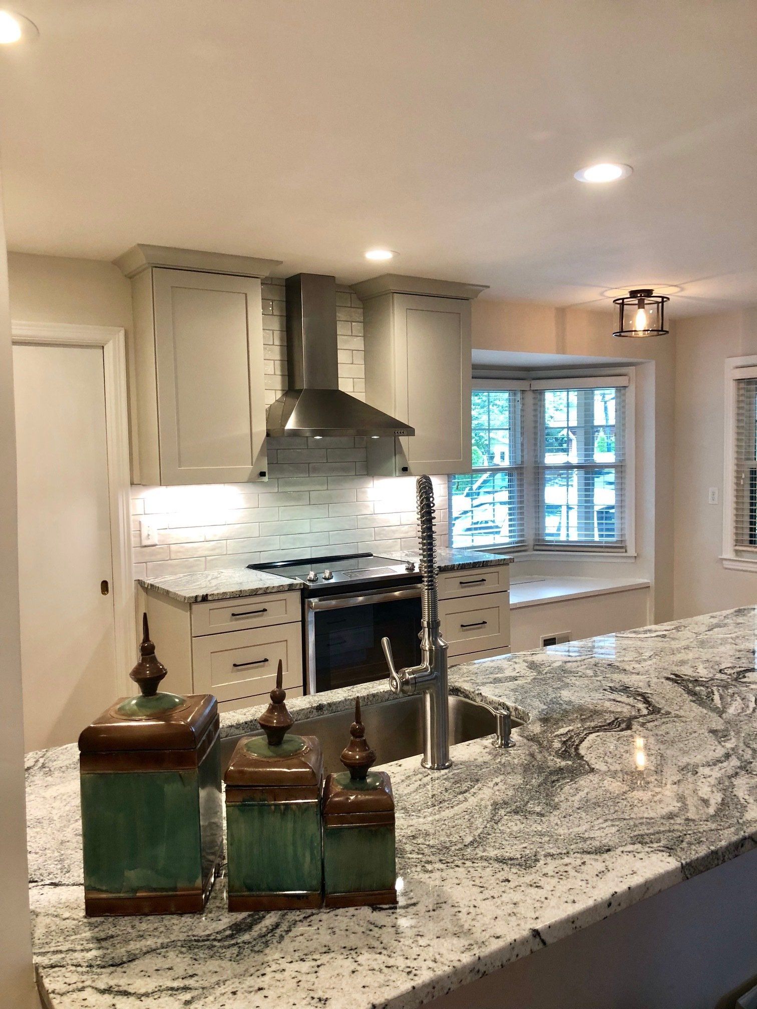 Kitchen with gray cabinets, granite countertops, stainless steel appliances, and decorative jars.