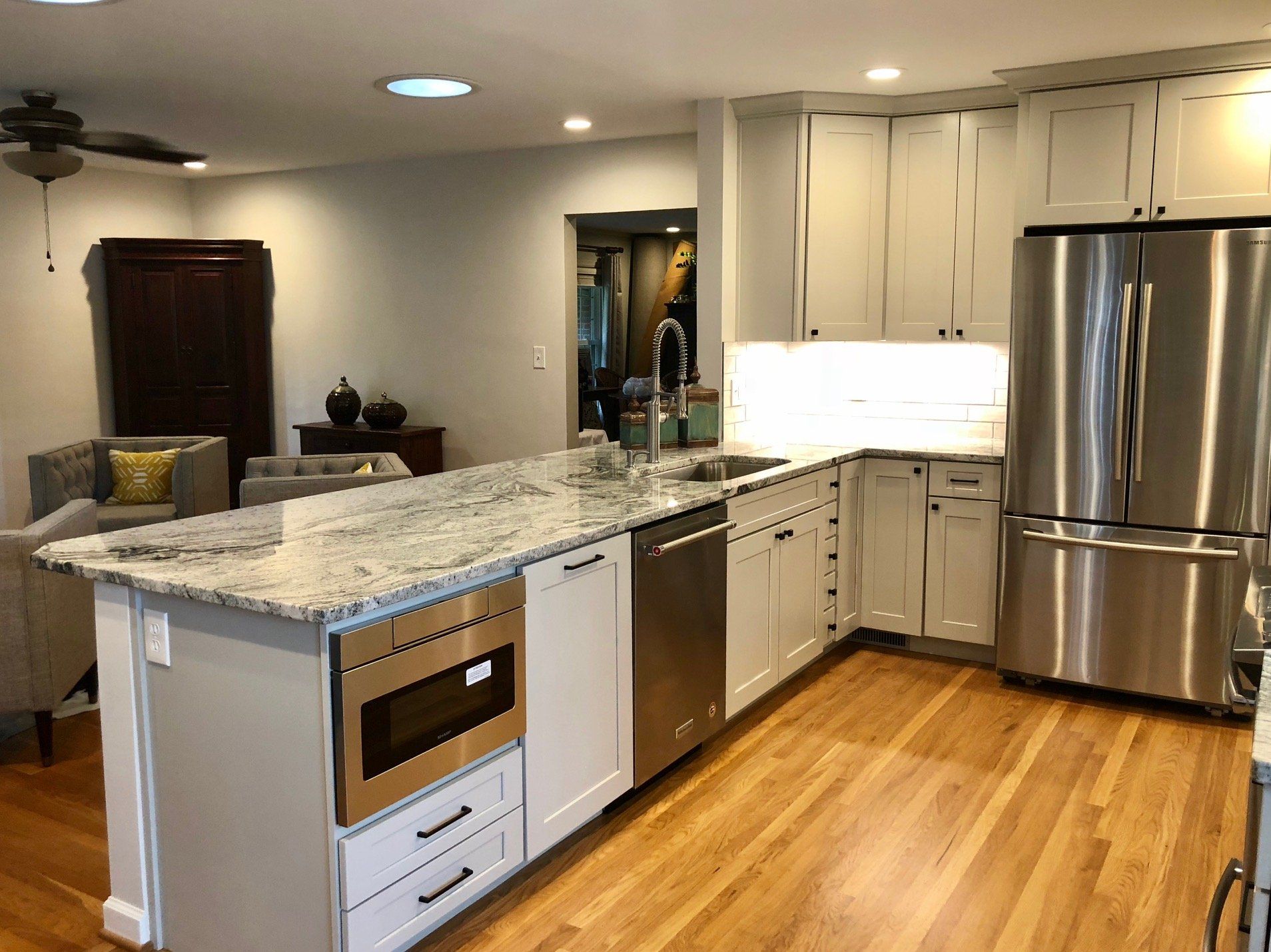 Modern kitchen with white cabinets, stainless steel appliances, granite countertops, and hardwood floors.