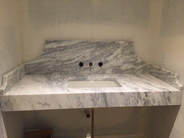 White marble bathroom vanity with sink, backsplash, and three faucet holes against beige walls