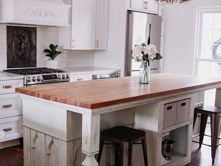 White kitchen with wood island, stainless steel appliances, and a vase of flowers.