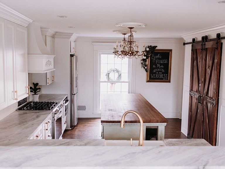 Elegant kitchen with white cabinets, wood island, chandelier, and a dark wooden sliding door.