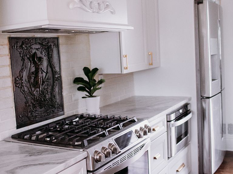 Modern kitchen with white cabinets, stainless steel appliances, and marble countertops.