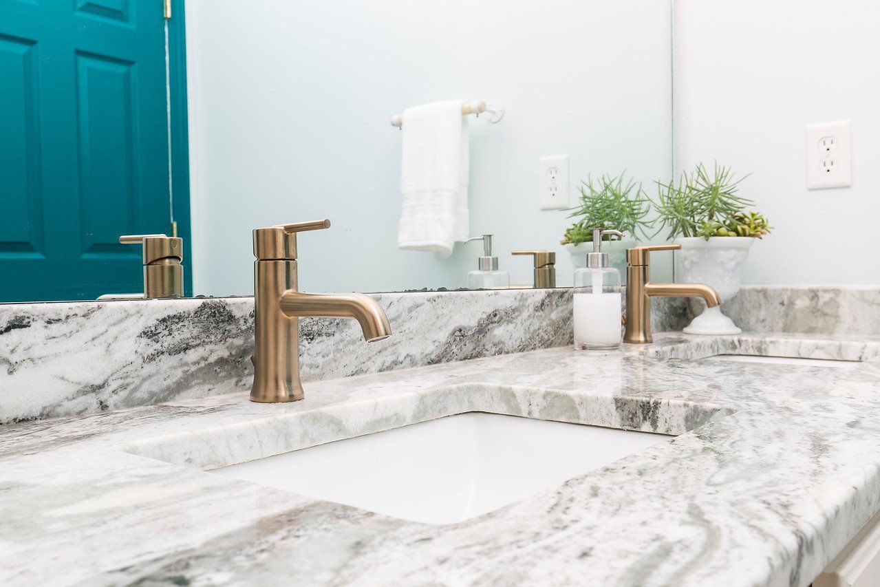 Modern bathroom sink with marble countertop, gold faucet, and teal door in the background
