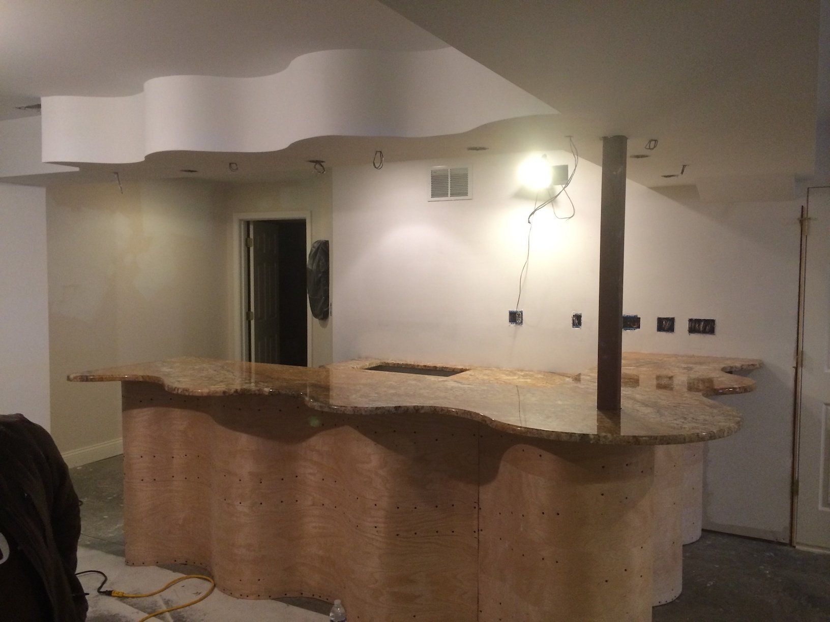 Basement bar with a wavy countertop and cabinetry. A wooden support post is in the middle.
