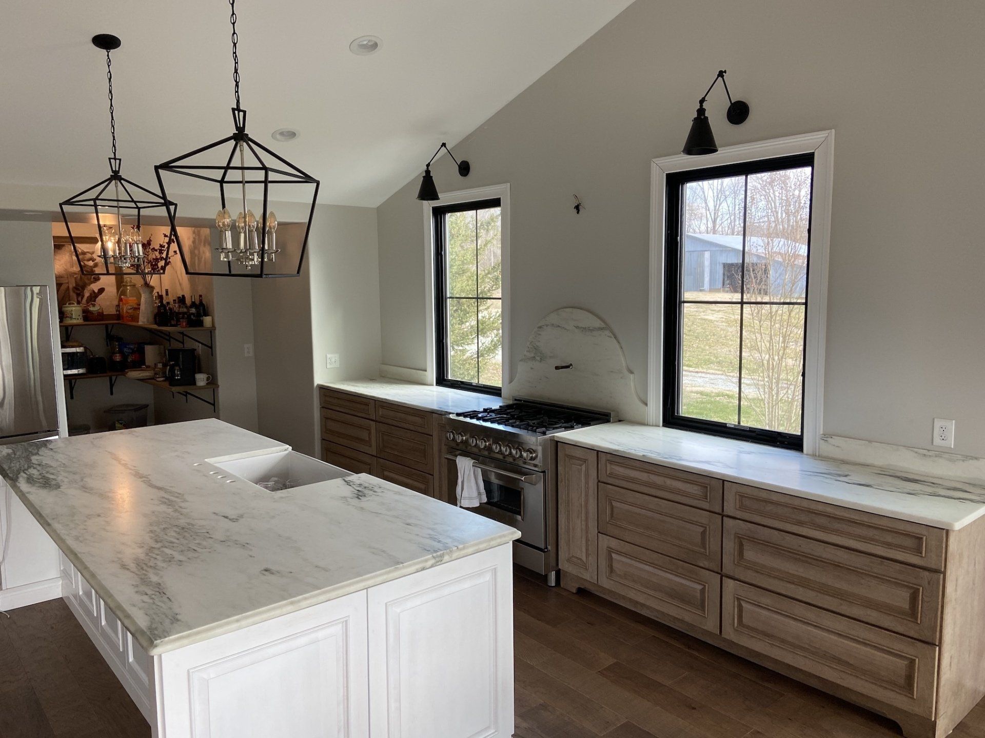 Spacious kitchen with a large island, wooden cabinets, and two windows. Neutral tones and modern lighting.